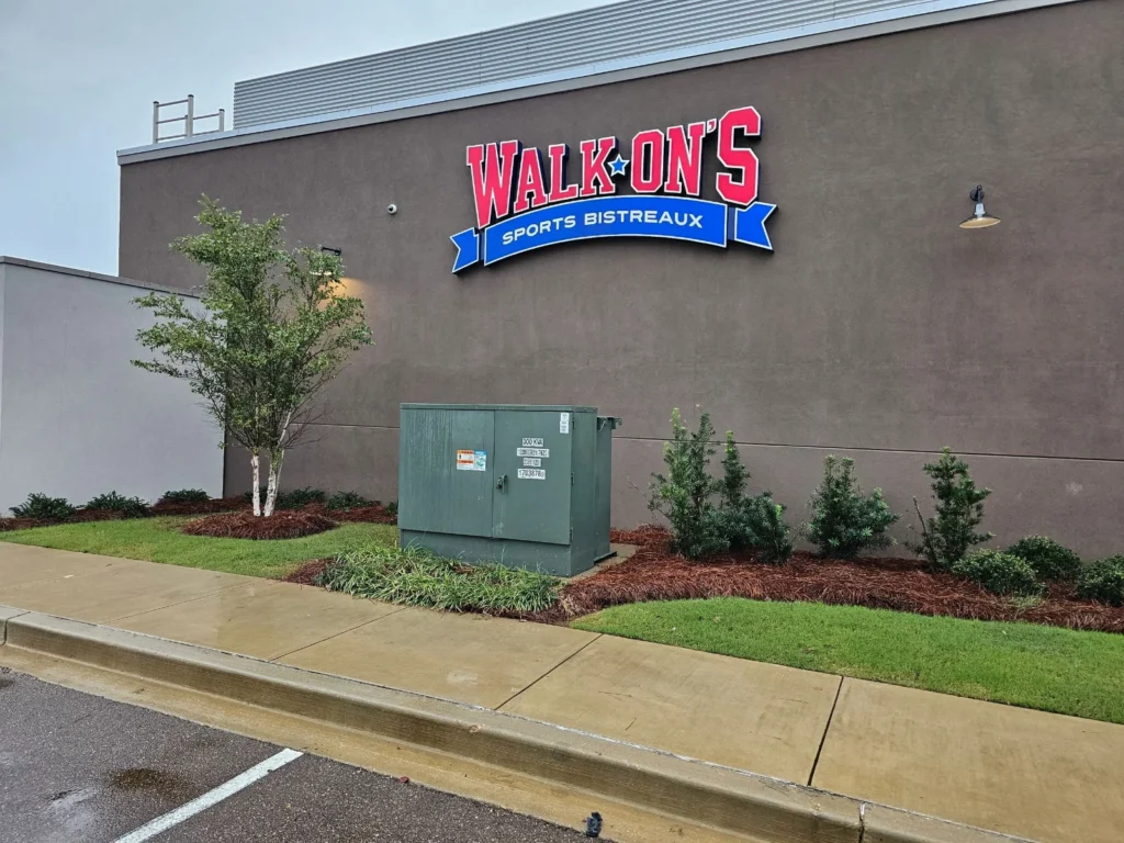 Exterior of a Walk-Ons Sports Bistreaux restaurant with a large logo on the wall and a green electrical utility box in the foreground.
