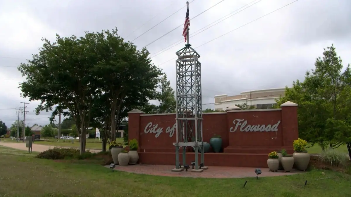 A red brick sign for the City of Flowood featuring a metal tower structure with a small American flag on top.